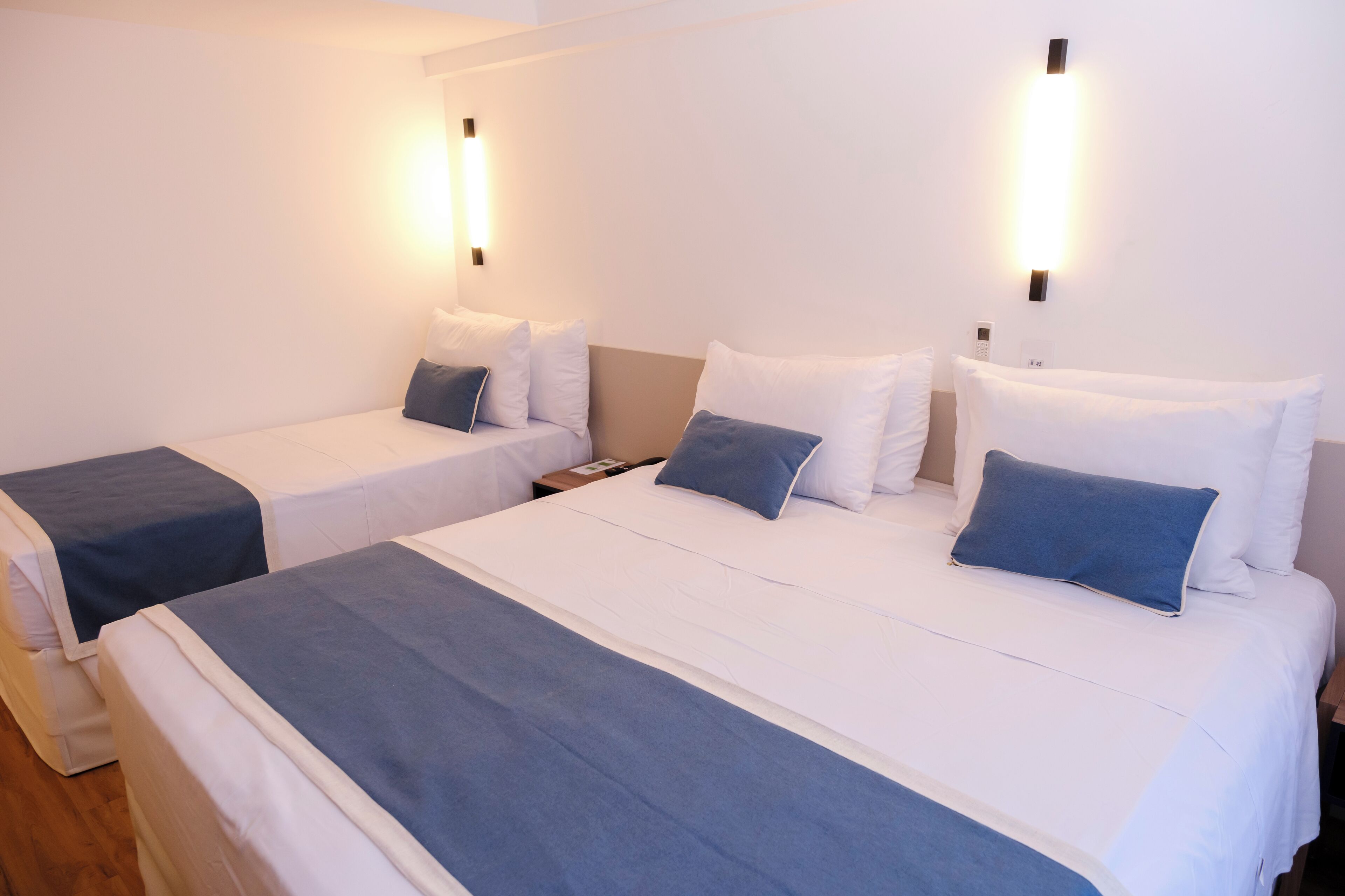 A hotel room with two beds, each with white bedding and blue accents, and bedside lamps.