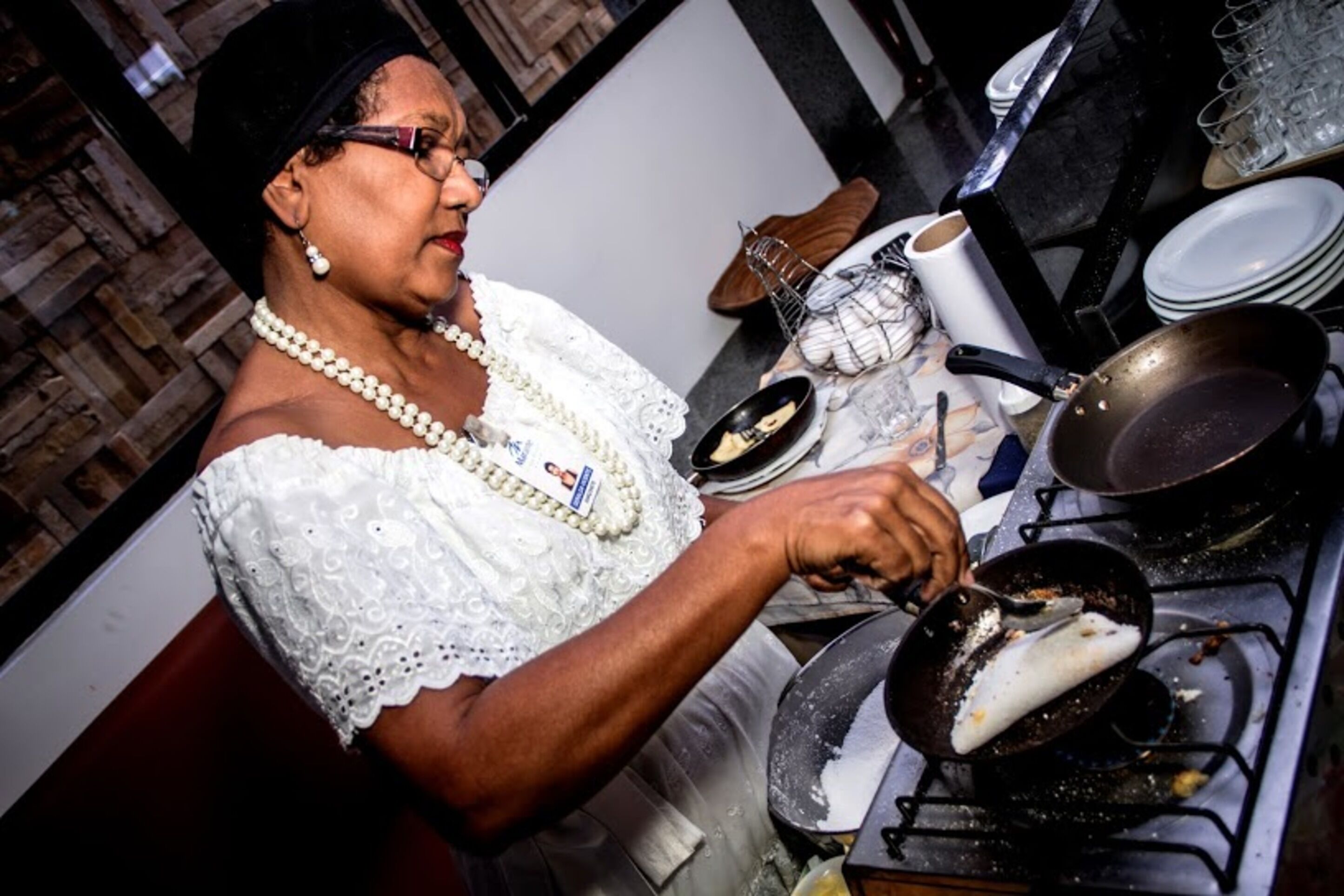 A person cooking in a kitchen with a stove, a frying pan, and various kitchen utensils.