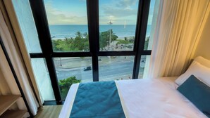 Een hotelkamer met een groot raam, met uitzicht op zee en een weg.