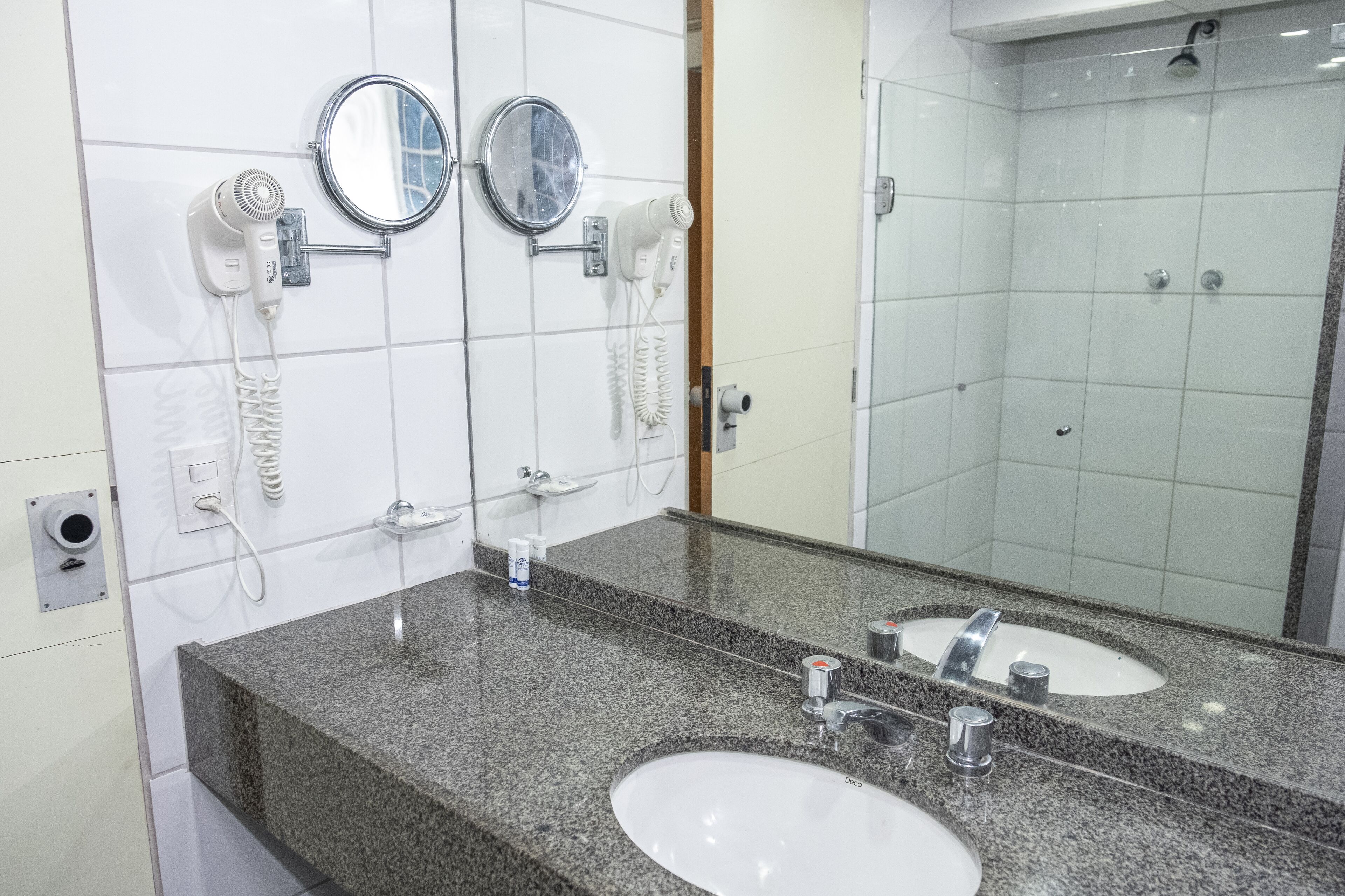 A bathroom with two sinks, a large mirror, and a hairdryer mounted on the wall.