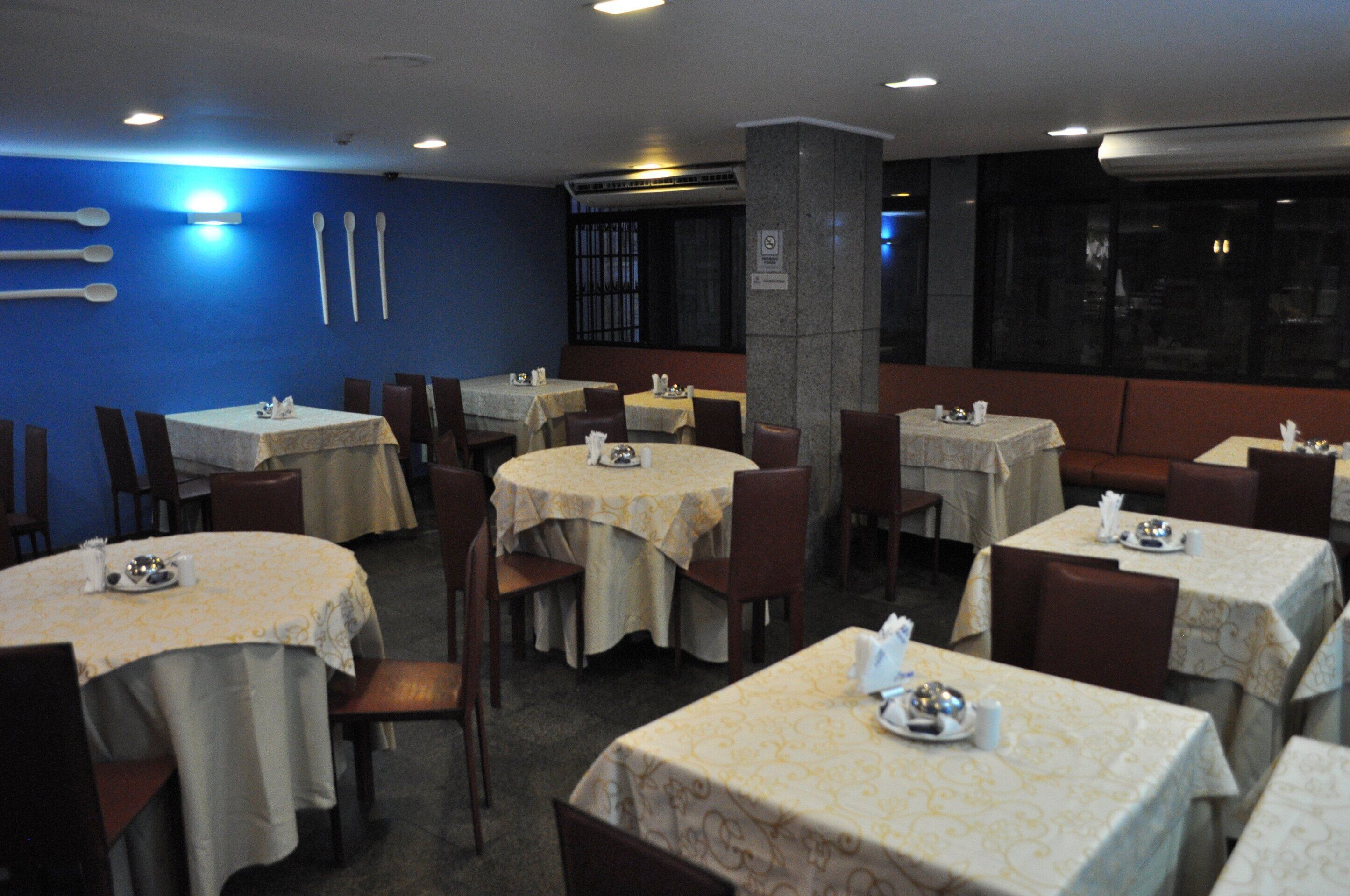 A restaurant with multiple tables and chairs, each set with a tablecloth and basic tableware.