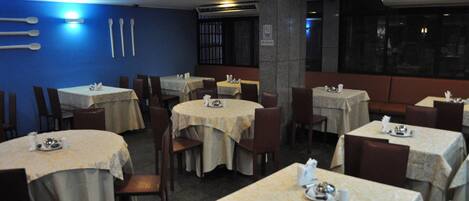 A restaurant with multiple tables and chairs, each set with a tablecloth and basic tableware.