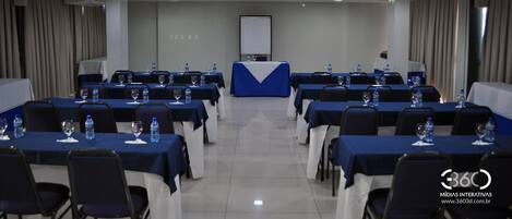 Un salón de conferencias con mesas dispuestas para una reunión, equipado con botellas de agua y vasos.