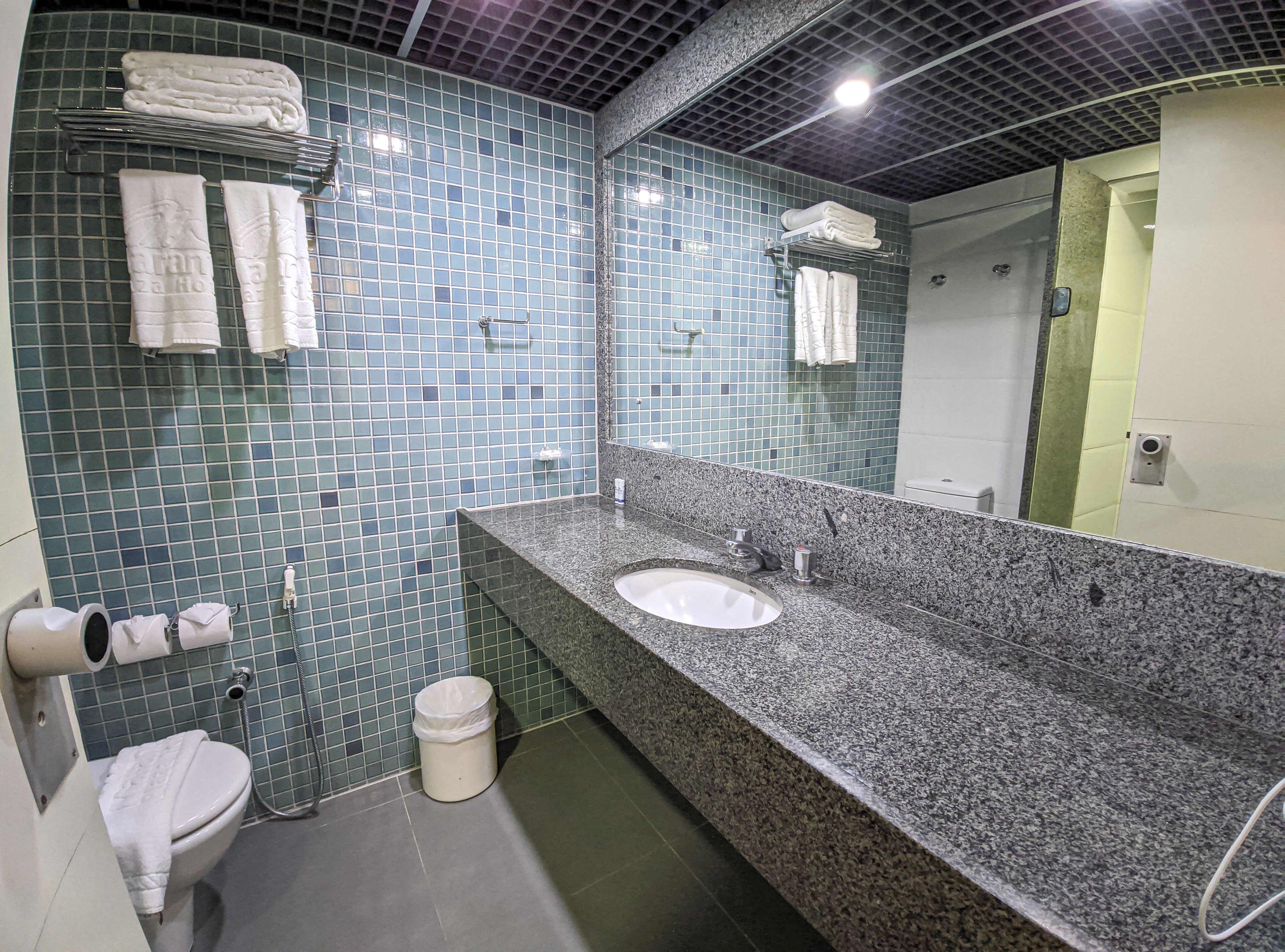 A bathroom with a granite countertop, two sinks, a toilet, and a shower.