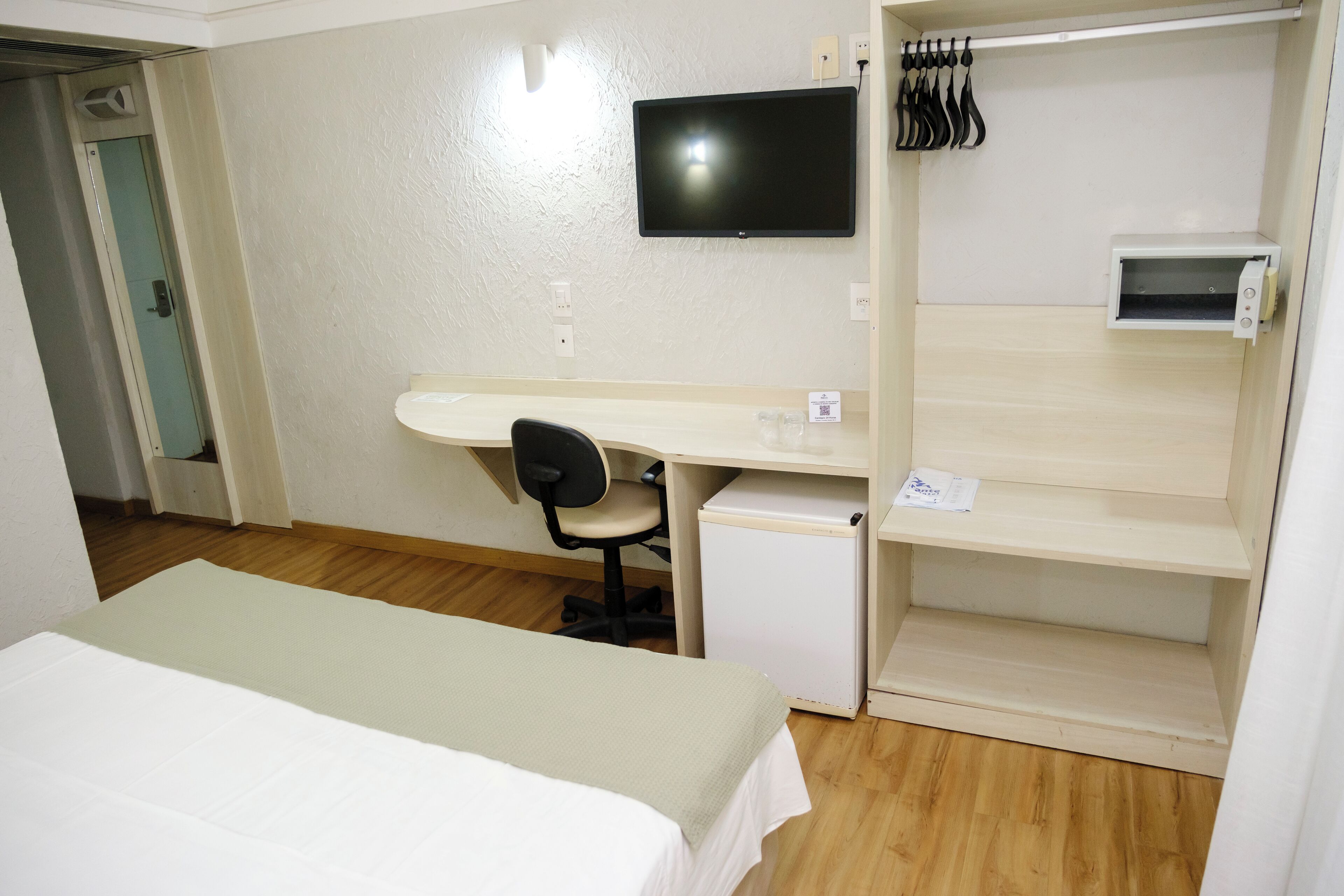 Ein Hotelzimmer mit Bett, Schreibtisch mit Stuhl, Fernseher und kleinem Kühlschrank.