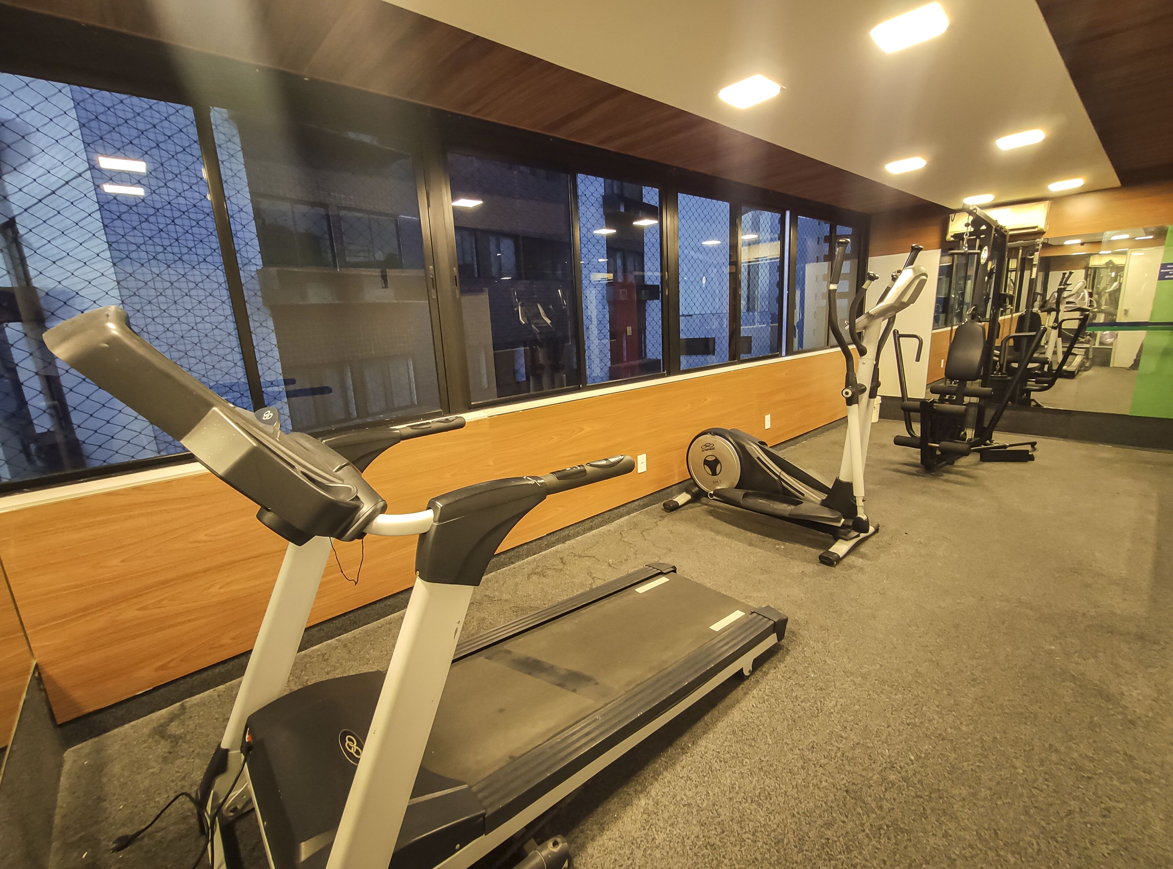 A gym with cardio equipment, wooden panels, and large windows.