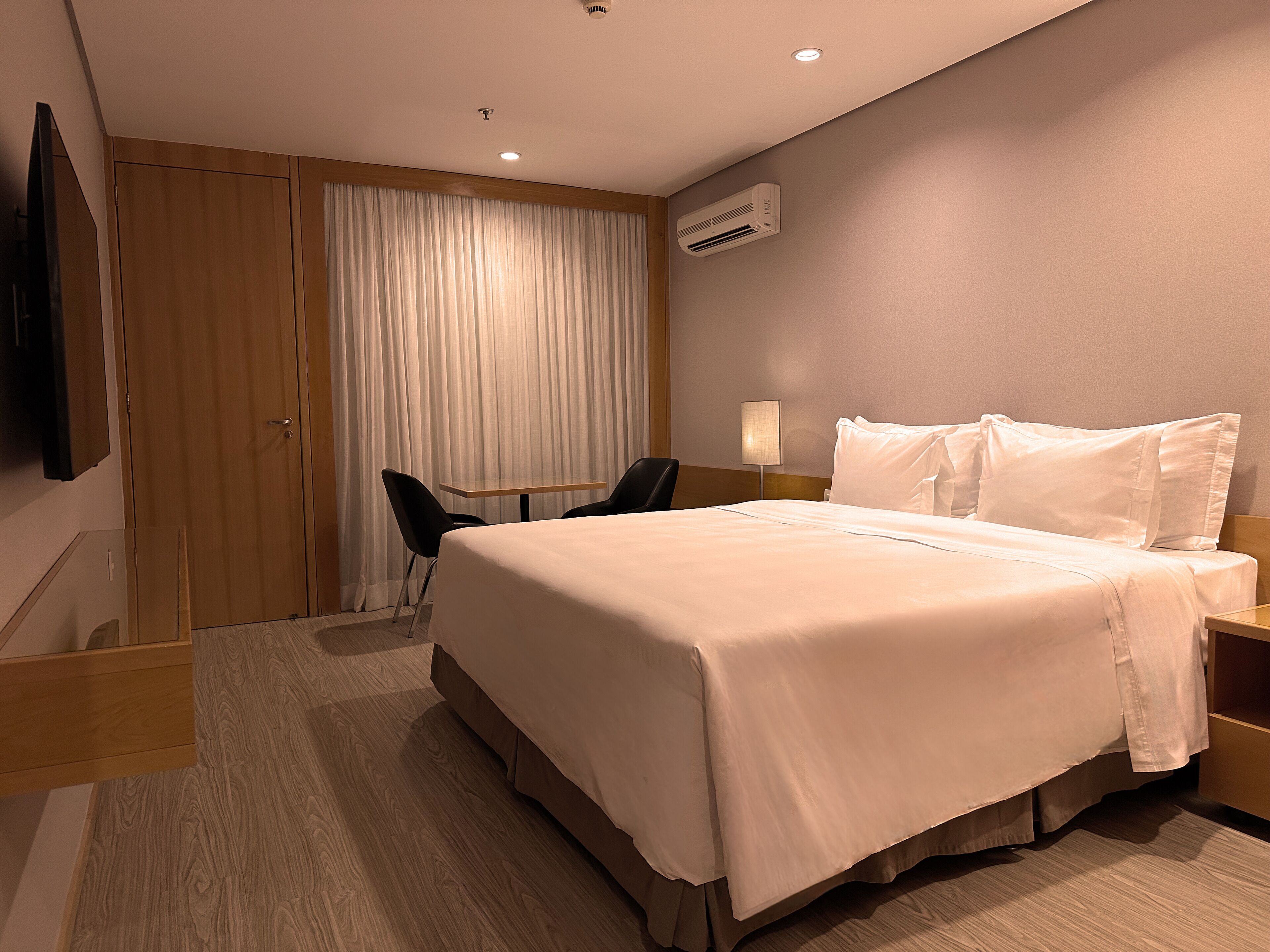 Habitación de hotel con una cama grande, un escritorio, una silla, un televisor y un aire acondicionado.