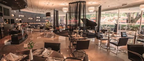 Un restaurante espacioso con varias áreas de comedor, un piano y vistas al exterior.