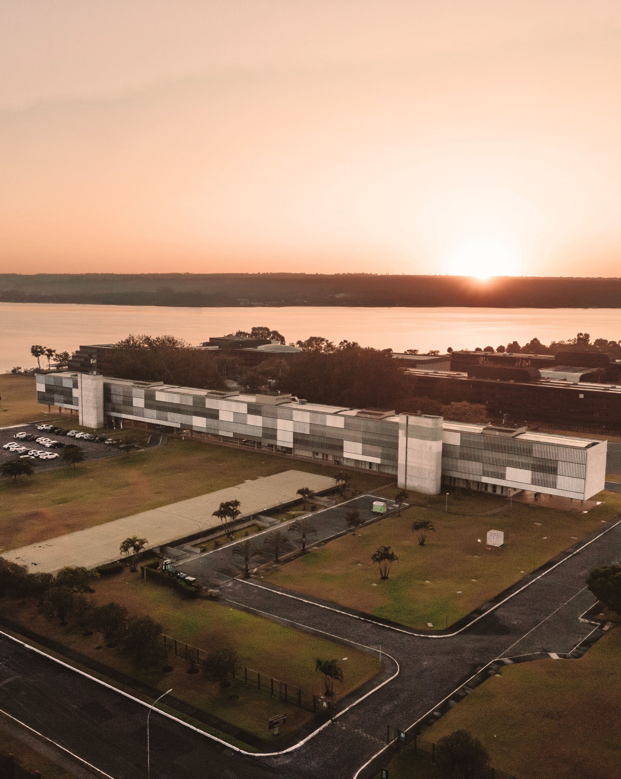 An aerial view of a modern building complex with a parking area and a road leading to it.