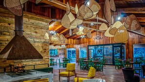 A rustic interior with wooden walls, a large fireplace, and green and yellow chairs.