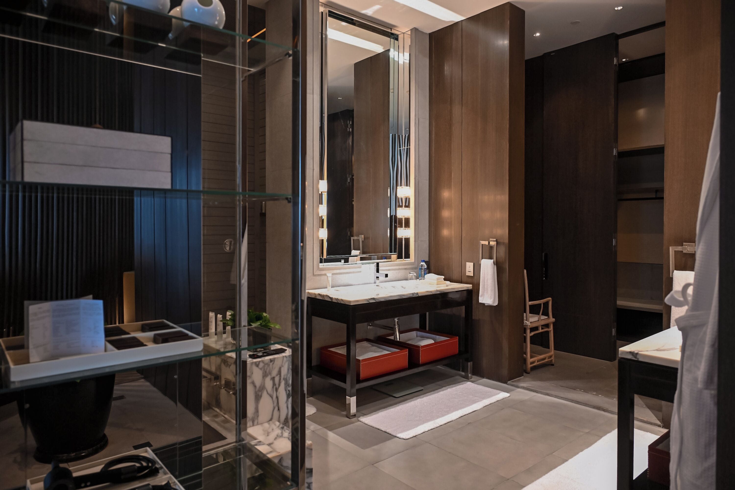 Un baño moderno con mampara de vidrio, tocador de madera, espejo grande y estante empotrado.