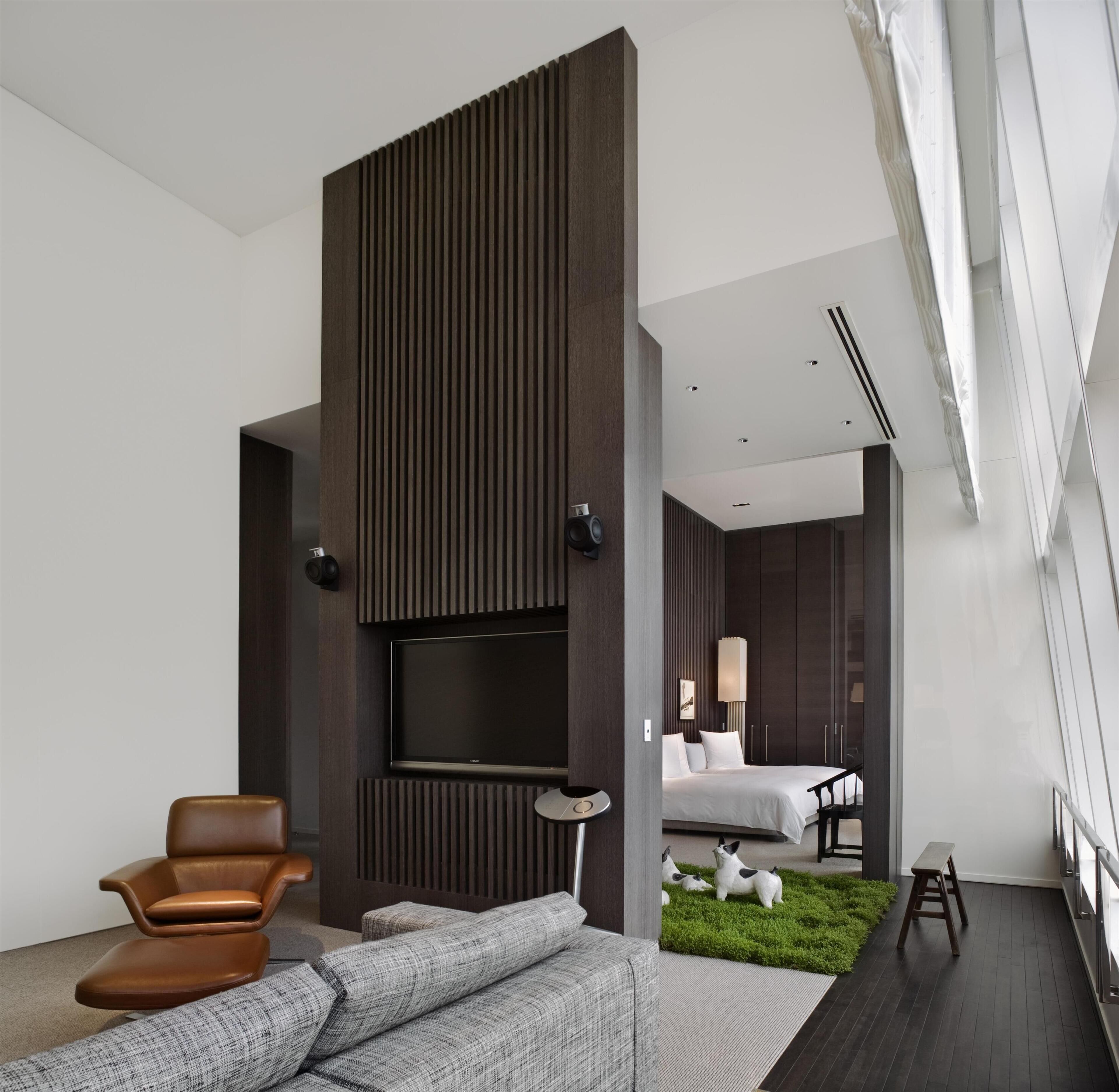 A modern hotel room with a large flat-screen TV, a sofa, a chair, a bed, and a small garden area.