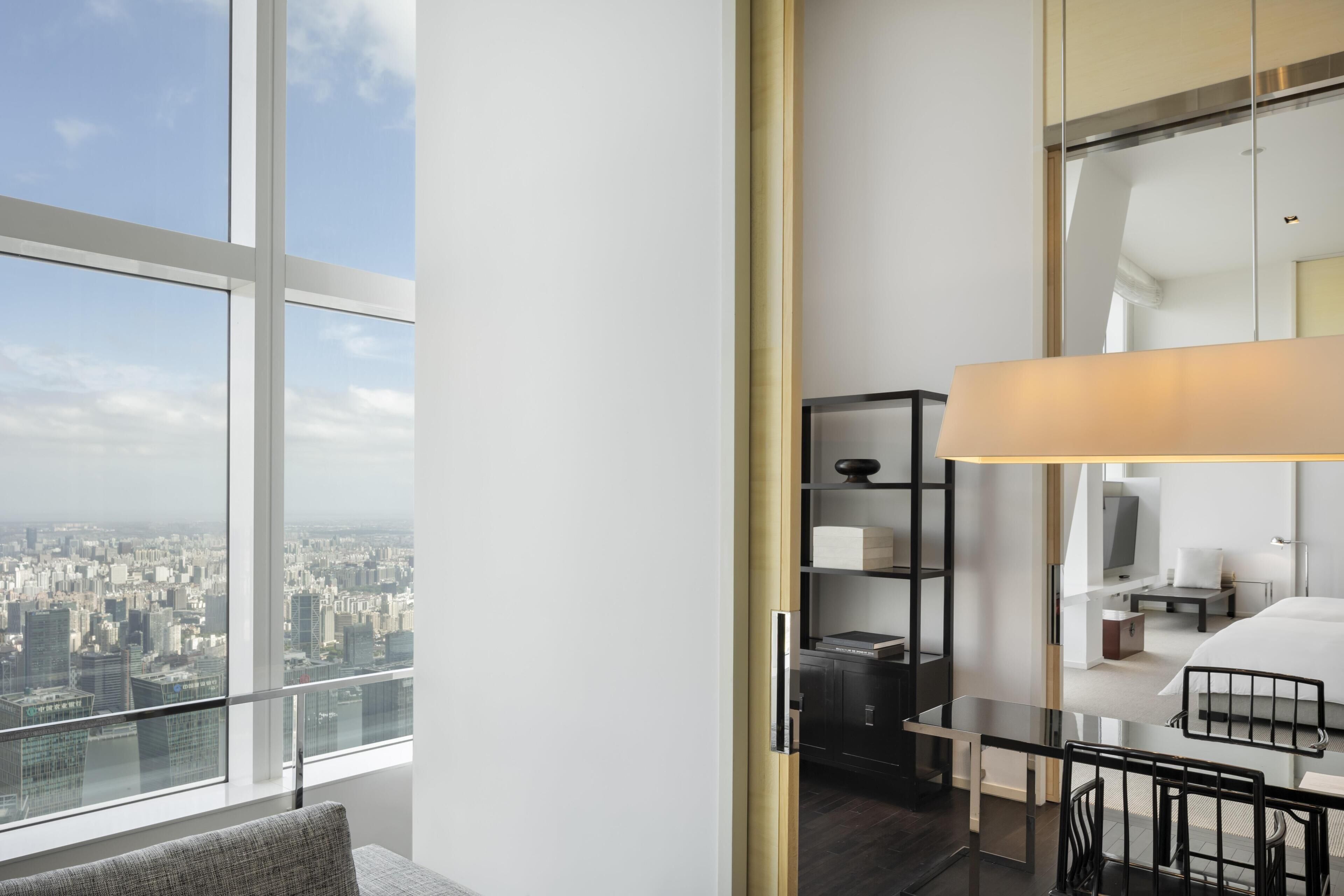 Una habitación de hotel moderna con vista a la ciudad, un escritorio, una silla, una lámpara y una cama.
