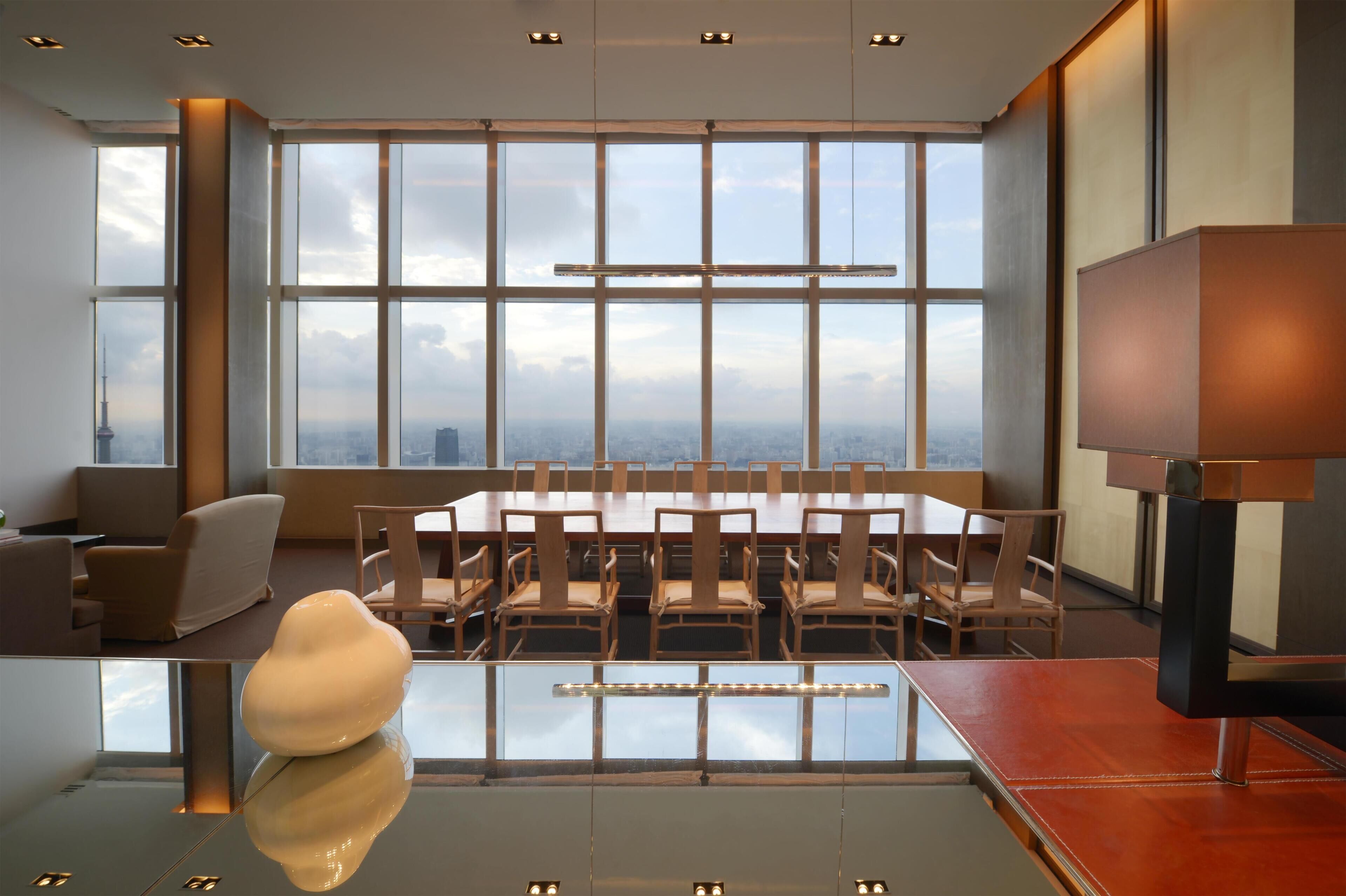 A modern conference room with a large table, chairs, and a view of a cityscape through large windows.