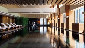 Una piscina interior moderna con sillones de descanso y una escalera que conduce a un nivel superior.