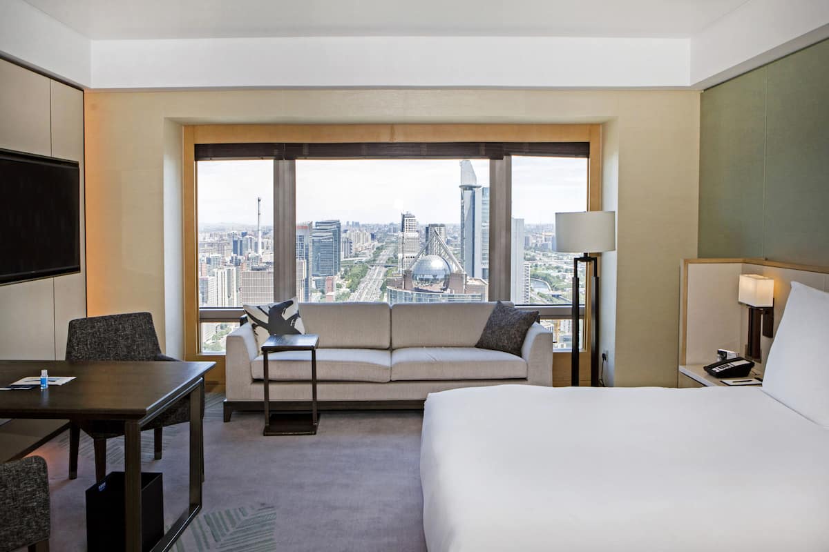 Une chambre d’hôtel dotée d’une grande fenêtre donnant sur la ville, d’un canapé, d’un lit, d’un bureau et d’une télévision.