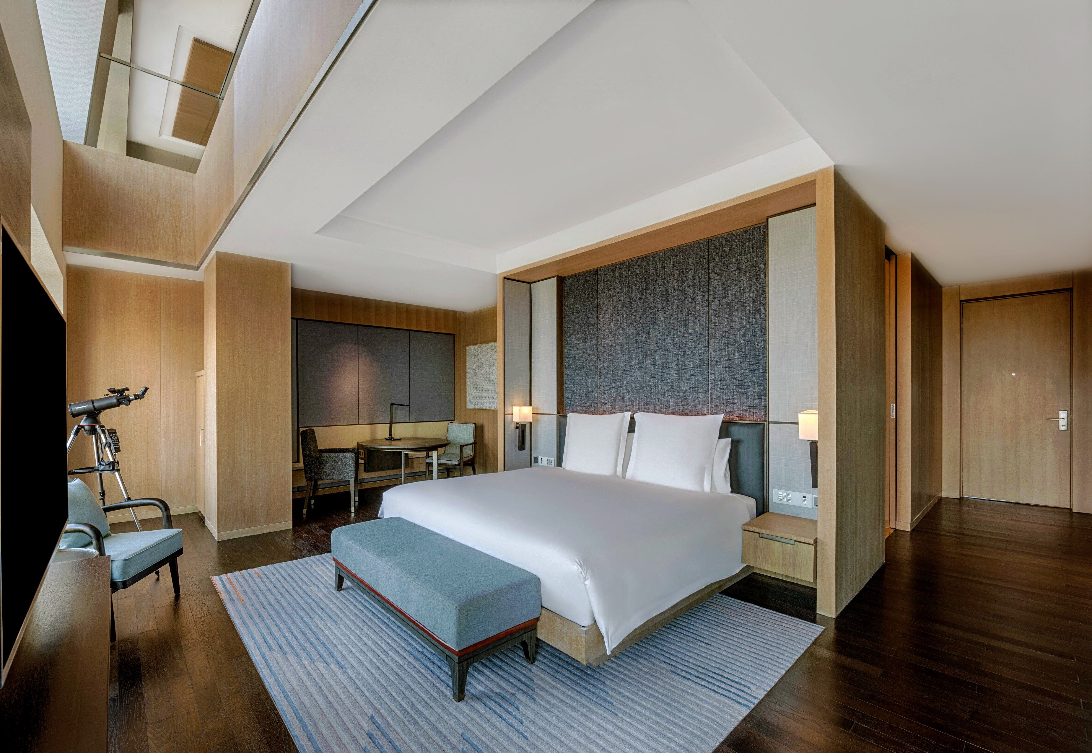 A modern hotel room with a large bed, a desk, a chair, and a small table.