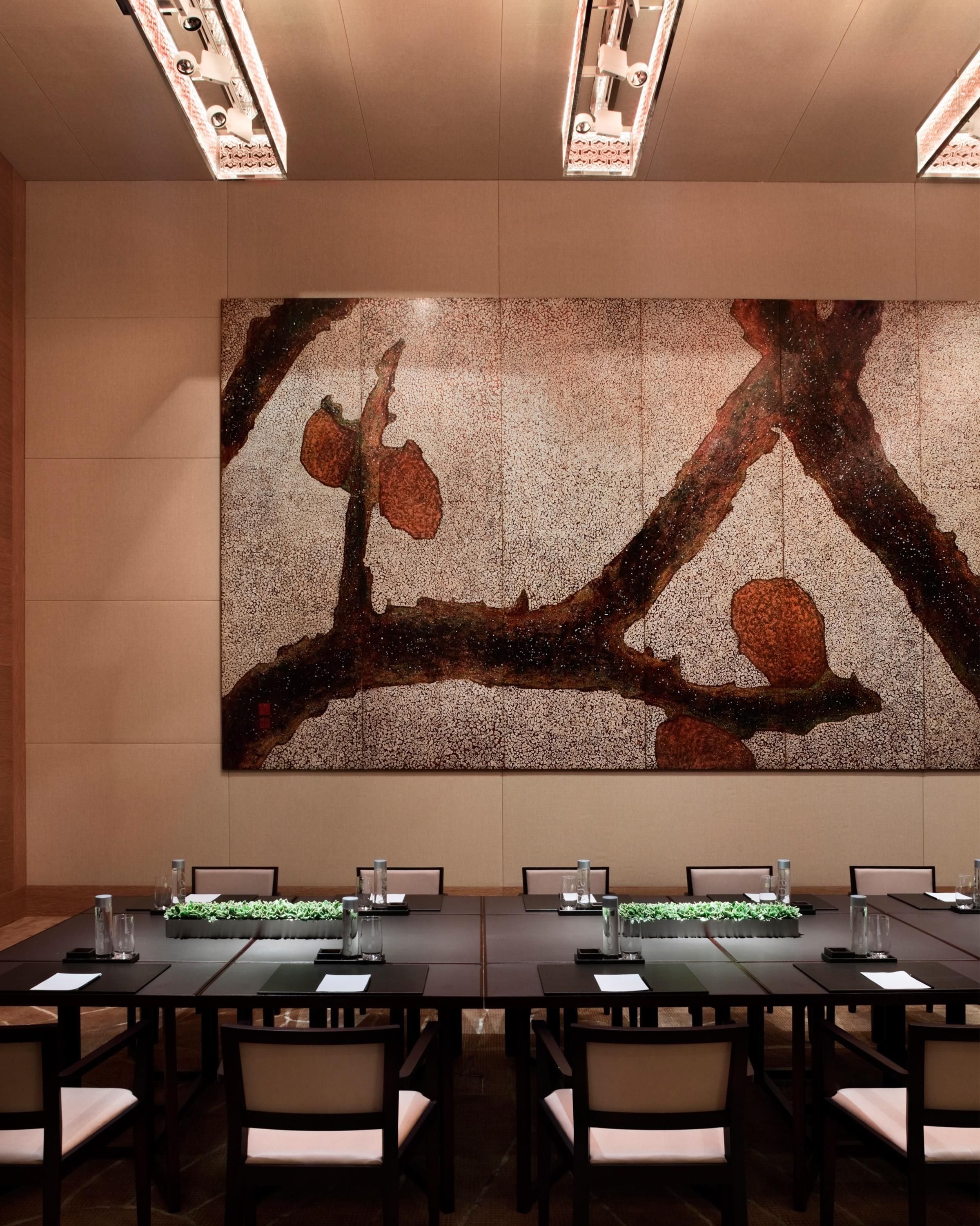 A conference room with a large abstract painting on the wall, a long table with chairs, and a plant on the table.