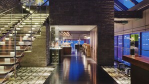 Un interior moderno con una escalera de cristal, una zona de estar central y vistas del cielo a través de un tragaluz.