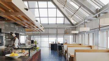 A modern restaurant with a high ceiling and large windows, featuring a central island with a chef preparing food.