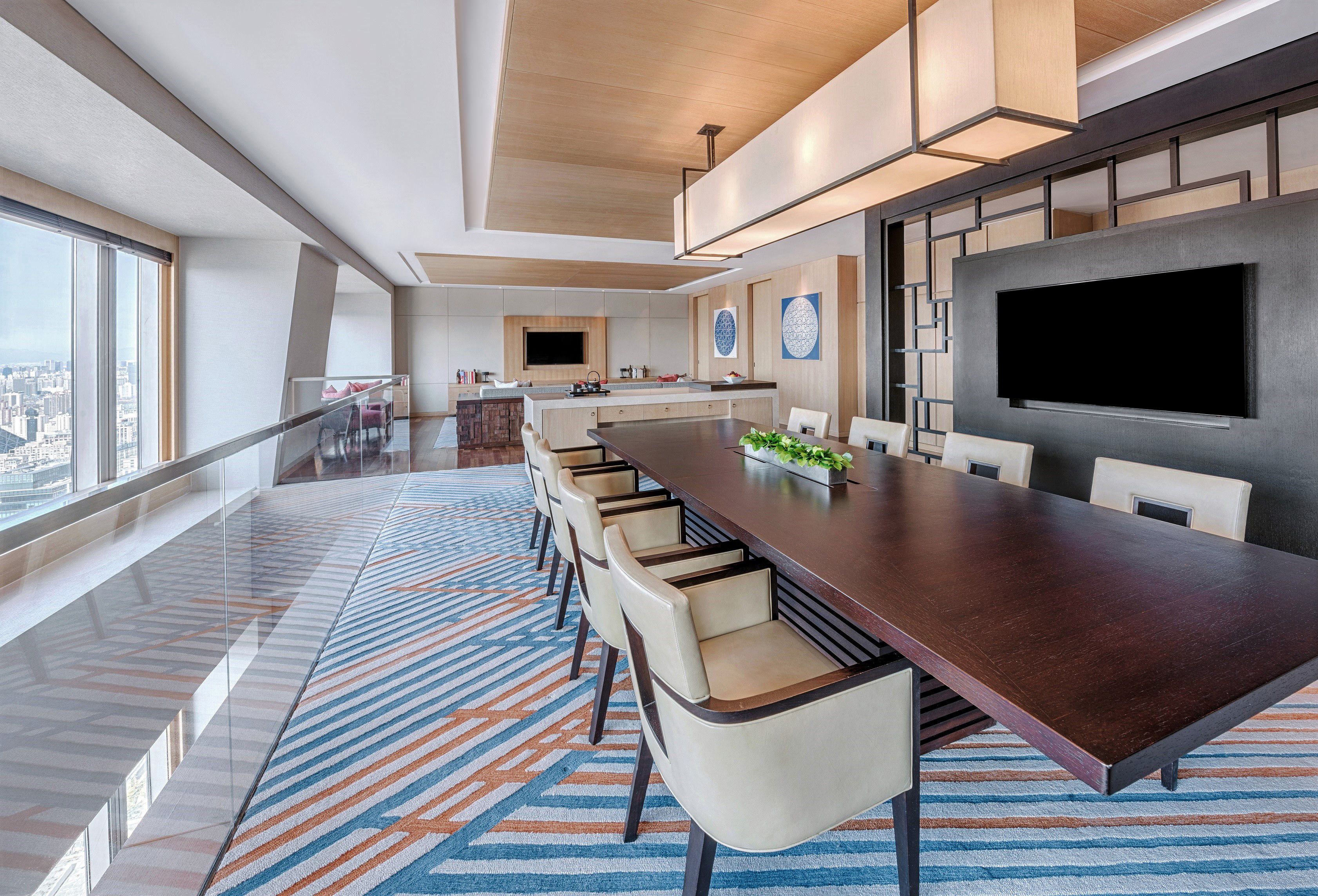 Una habitación de hotel moderna con una amplia mesa de comedor, asientos cómodos, una cocina y un gran ventanal con vistas a la ciudad.