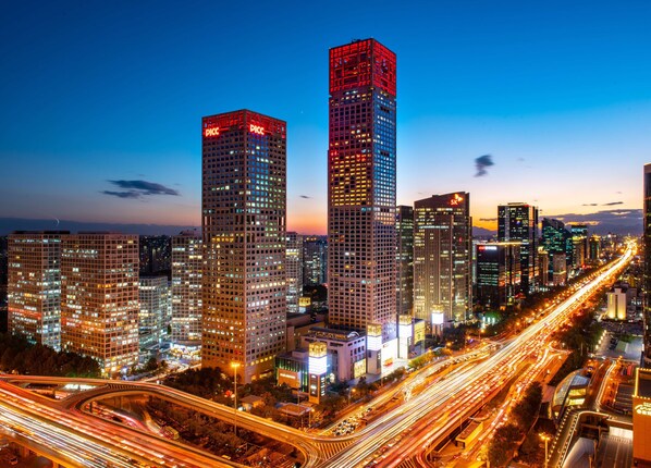 A cityscape with high-rise buildings, including a prominent skyscraper with illuminated signage. - Park Hyatt Beijing (Beijing)