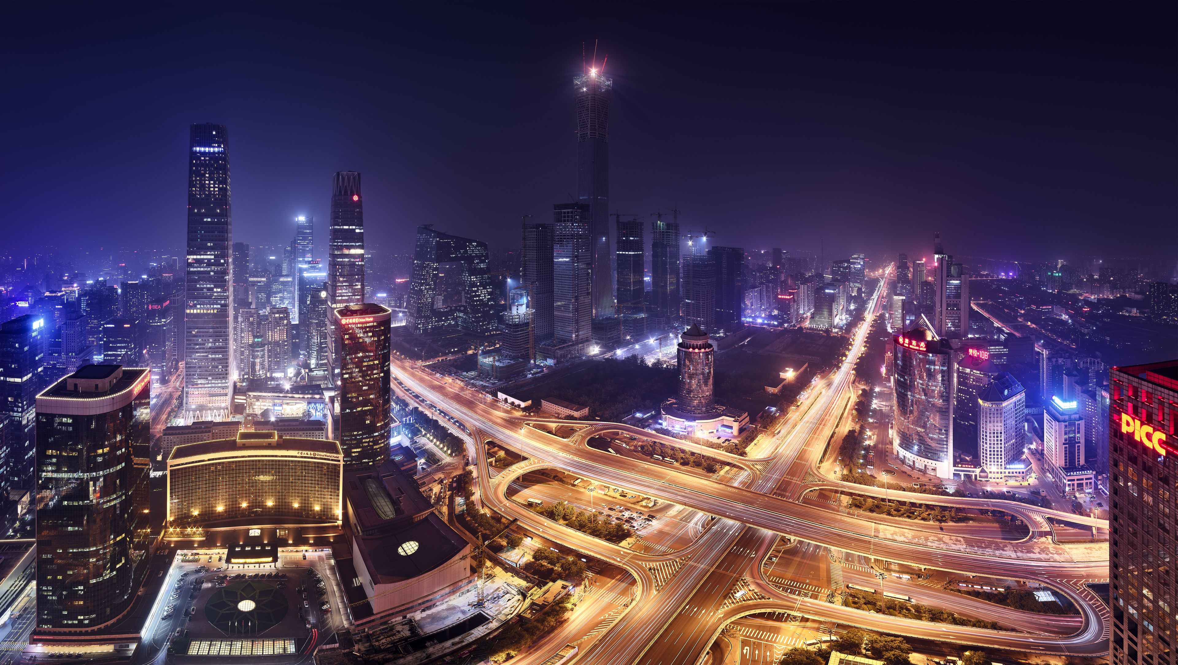 A nighttime cityscape with illuminated skyscrapers and a complex highway interchange.