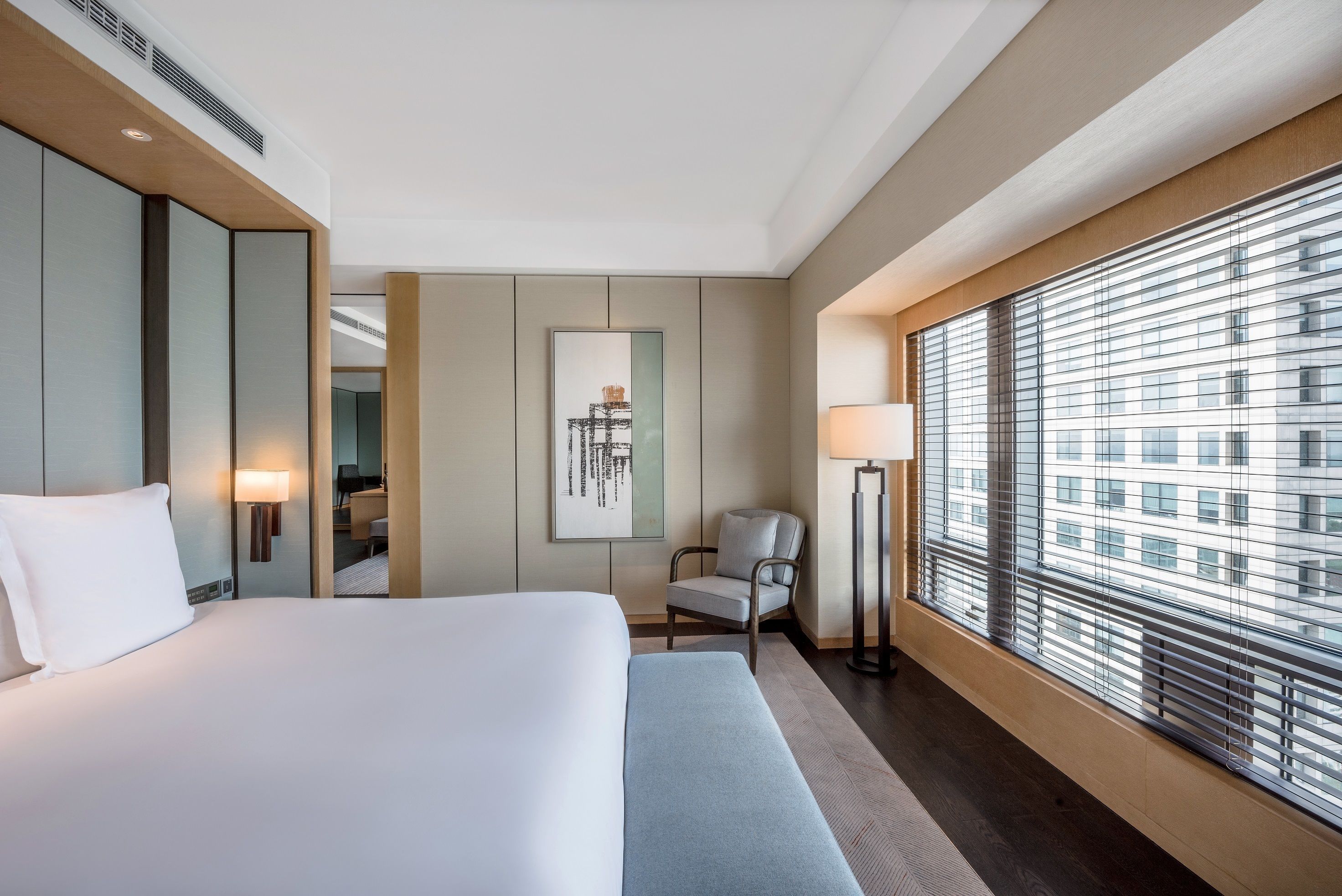 A hotel room with a large bed, a chair, a desk, and a window with blinds.