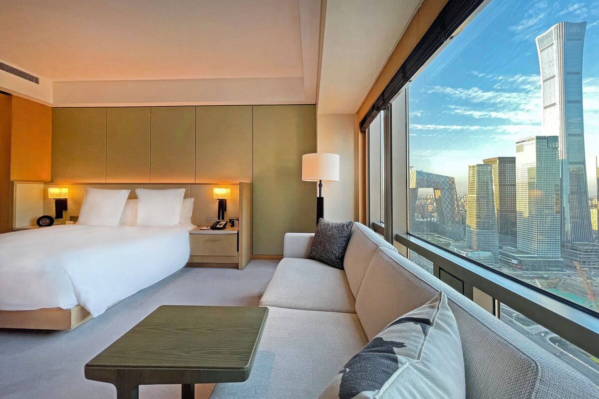 Une chambre d’hôtel équipée d’un lit, d’un canapé, d’une table et d’une grande fenêtre donnant sur la ville.