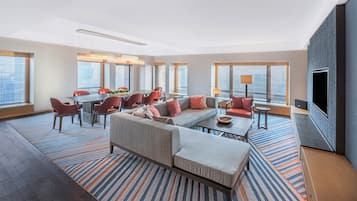 A modern hotel room with a large sofa, dining area, and a flat-screen TV.