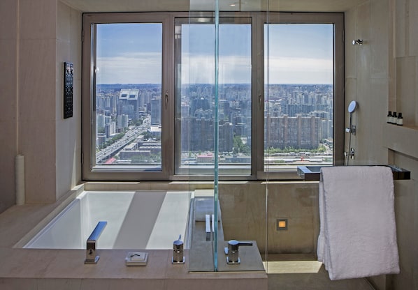 A modern bathroom with a large window, a bathtub, a shower, and a towel rack.