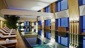 Un área de piscina interior moderna con sillones de descanso y una barrera de vidrio.
