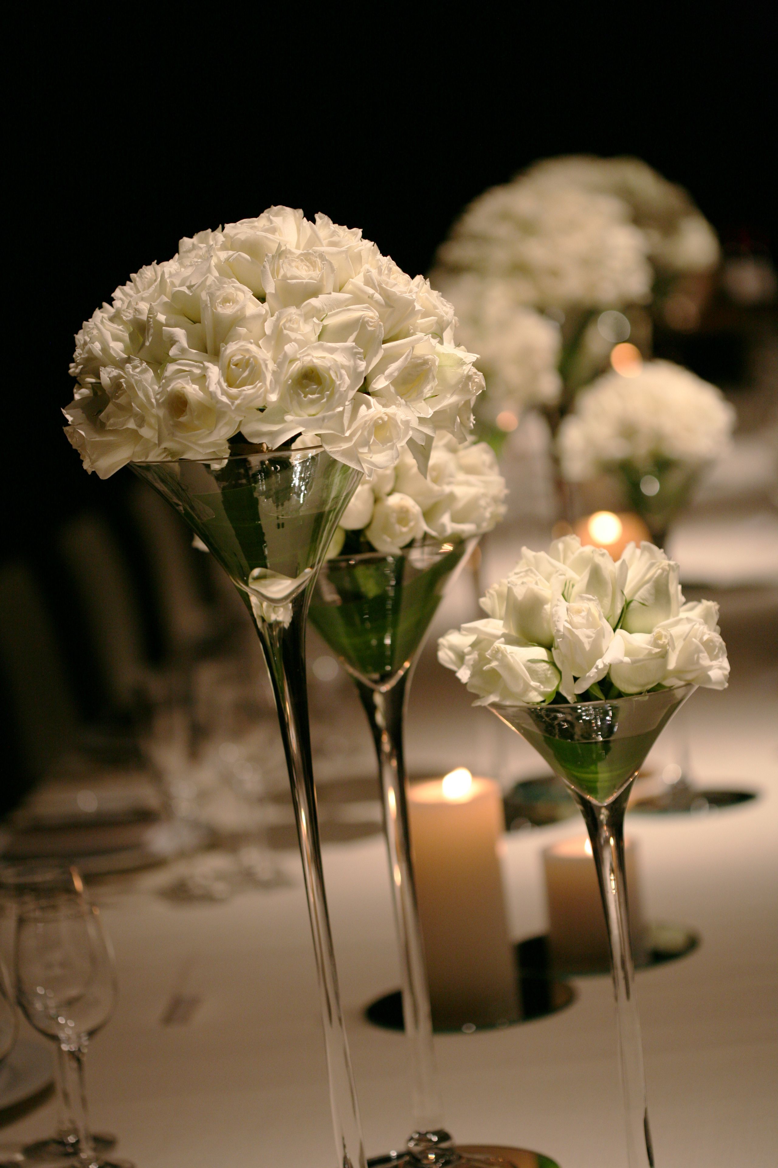 A table with white flowers in martini glasses, candles, and a glass of water.