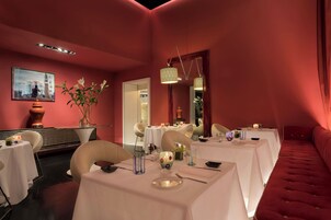 Un espace repas avec des tables dressées pour le service, un miroir et un banc recouvert d’un tissu rouge.