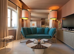 Uma sala de estar moderna com um sofá azul-turquesa, uma mesa de centro com uma bandeja de itens de café da manhã e uma TV de tela plana na parede.