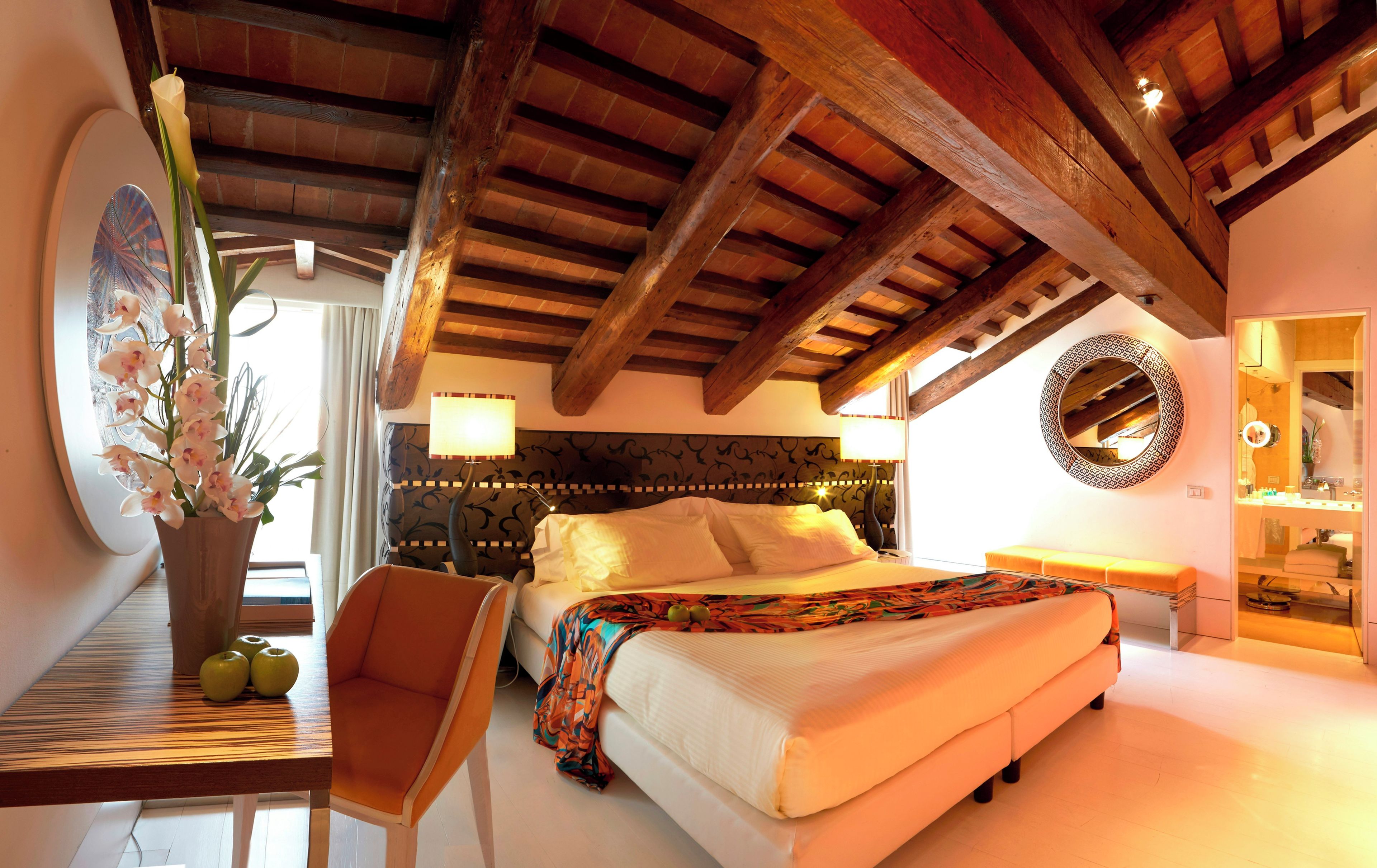 Un dormitorio con una cama, una silla, una mesa con manzanas y una orquídea en maceta.