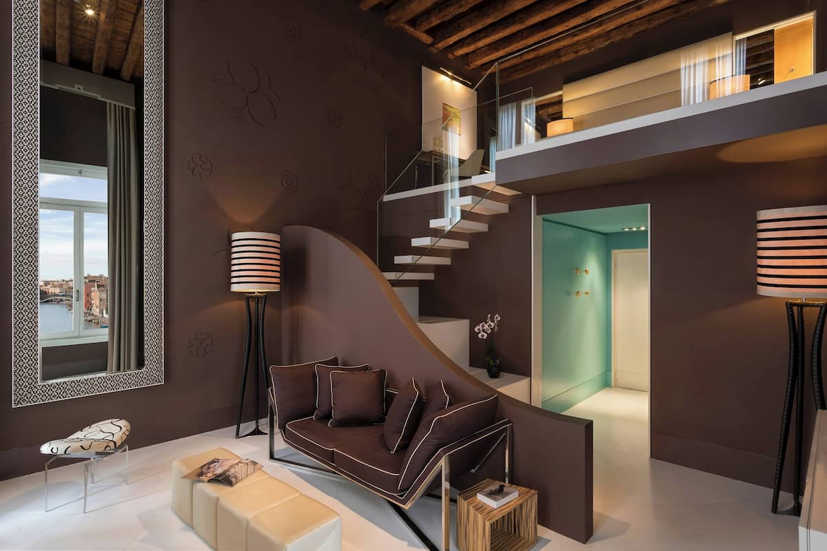 Un interior moderno con un sofá curvo, una escalera de cristal y vistas a un paisaje urbano a través de una ventana.
