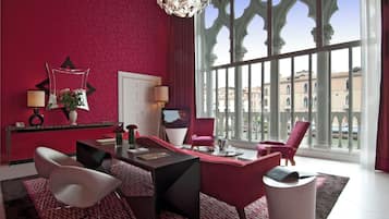 Una habitación de hotel moderna con una pared roja, un ventanal con vistas a edificios, un escritorio con una computadora y dos sillas.