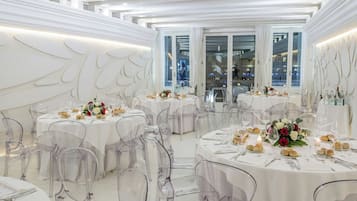 A spacious, elegantly decorated dining area with round tables, clear chairs, and white drapery.