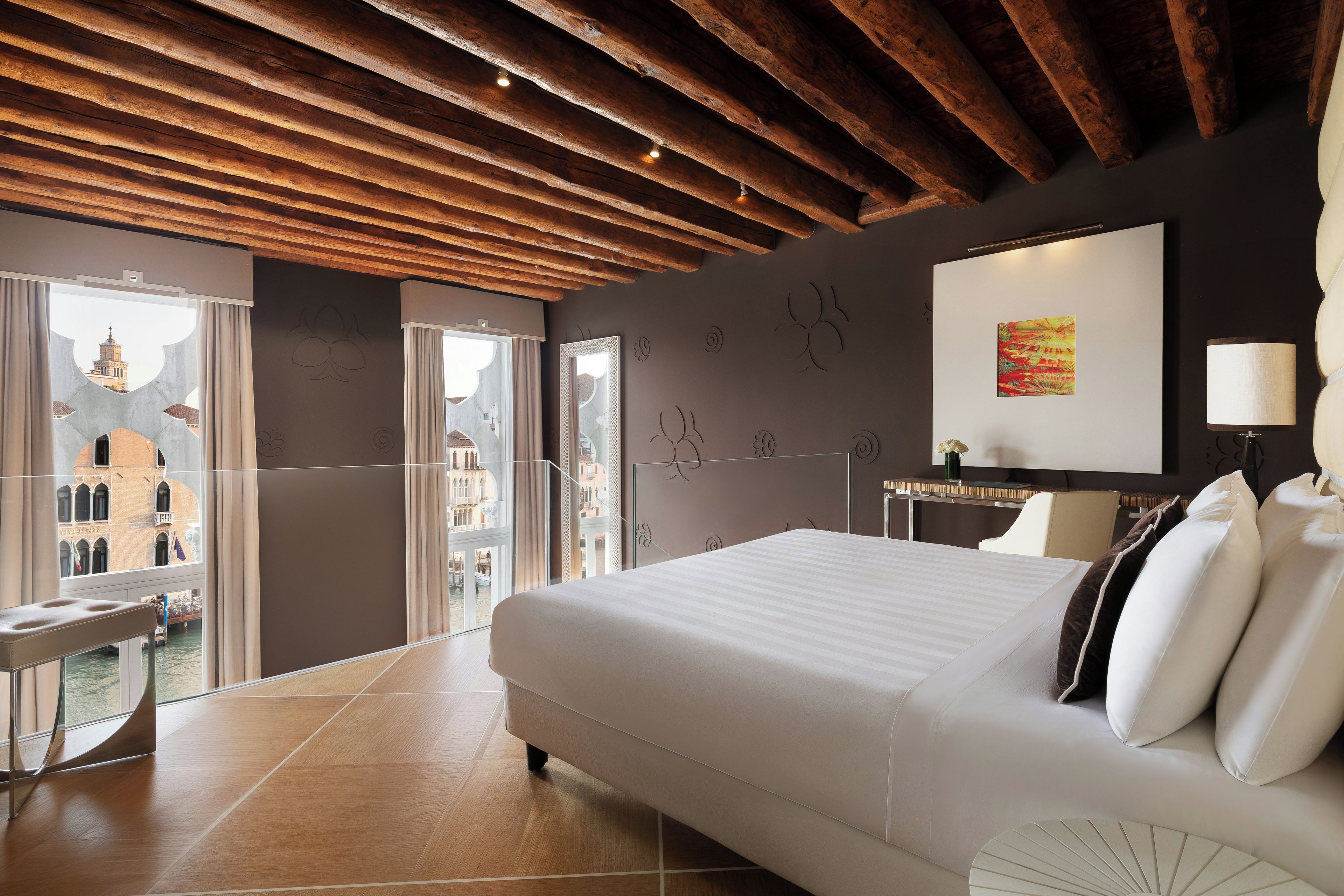 A hotel room with a bed, a desk, a chair, and a view of a cityscape.