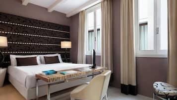A hotel room with a bed, bedside table, lamp, chair, and a desk with books.