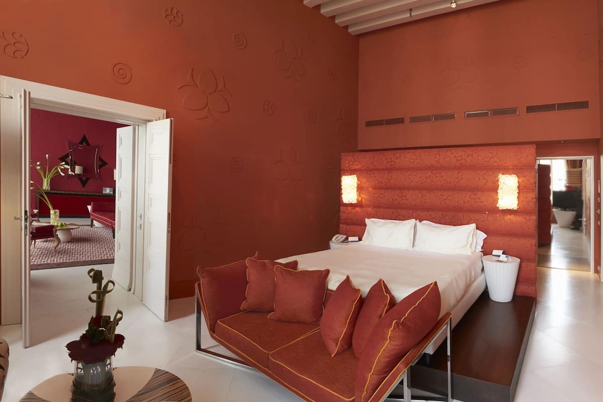 Un dormitorio moderno con una cama grande, un sofá rojo y una mesita con un florero.