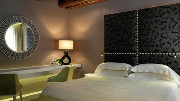 A hotel room with a large bed, a round mirror, a bedside table with a lamp, and a green bench.