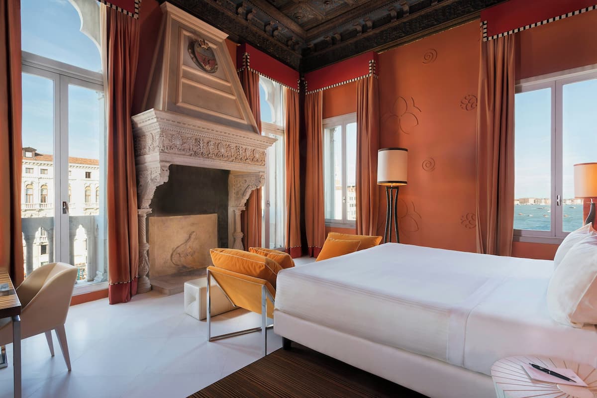 Habitación de hotel con una cama grande, chimenea, vistas de la ciudad y un escritorio con silla.