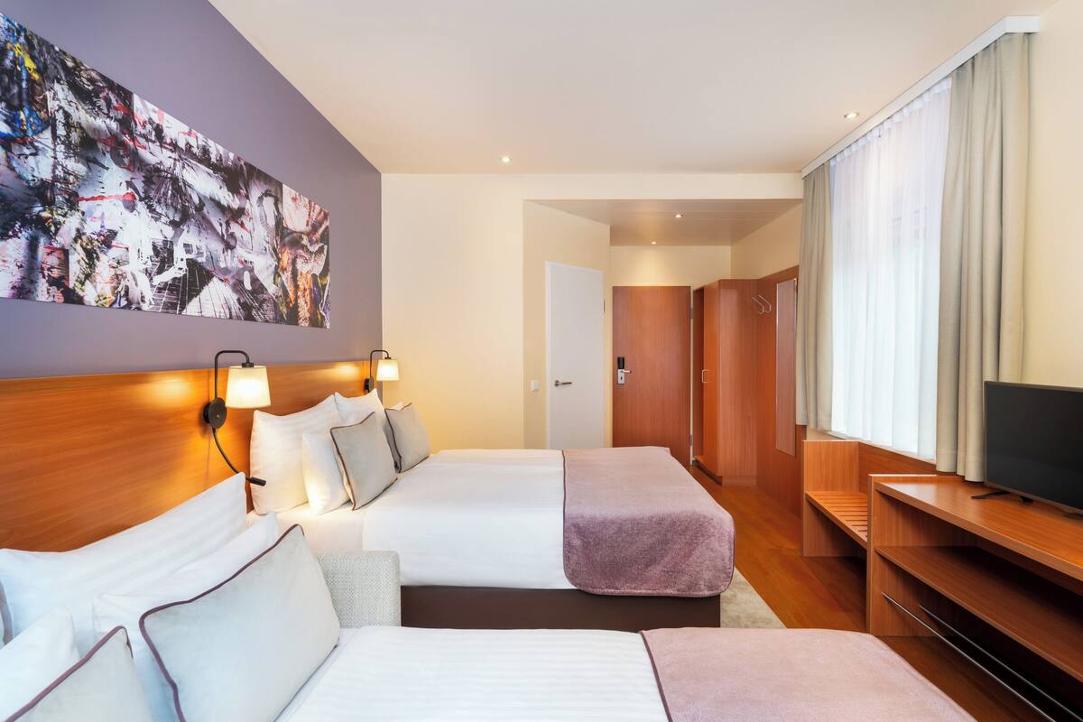 A hotel room with two beds, a TV, a painting on the wall, and a door leading to another room.