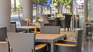 An outdoor seating area with wicker furniture and a wooden table, featuring a vase with flowers. -  Leonardo Hotel Salzburg City Center (Salzburg)