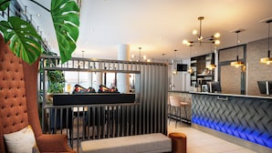 A modern hotel lobby with a bar area, seating, and a large plant. -  Leonardo Hotel Salzburg City Center (Salzburg)