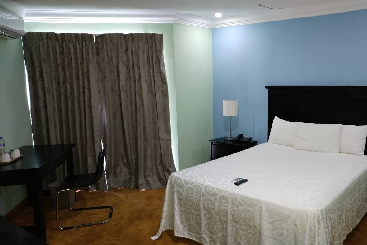 Een hotelkamer met een bed, nachtkastje, lamp en een stoel.