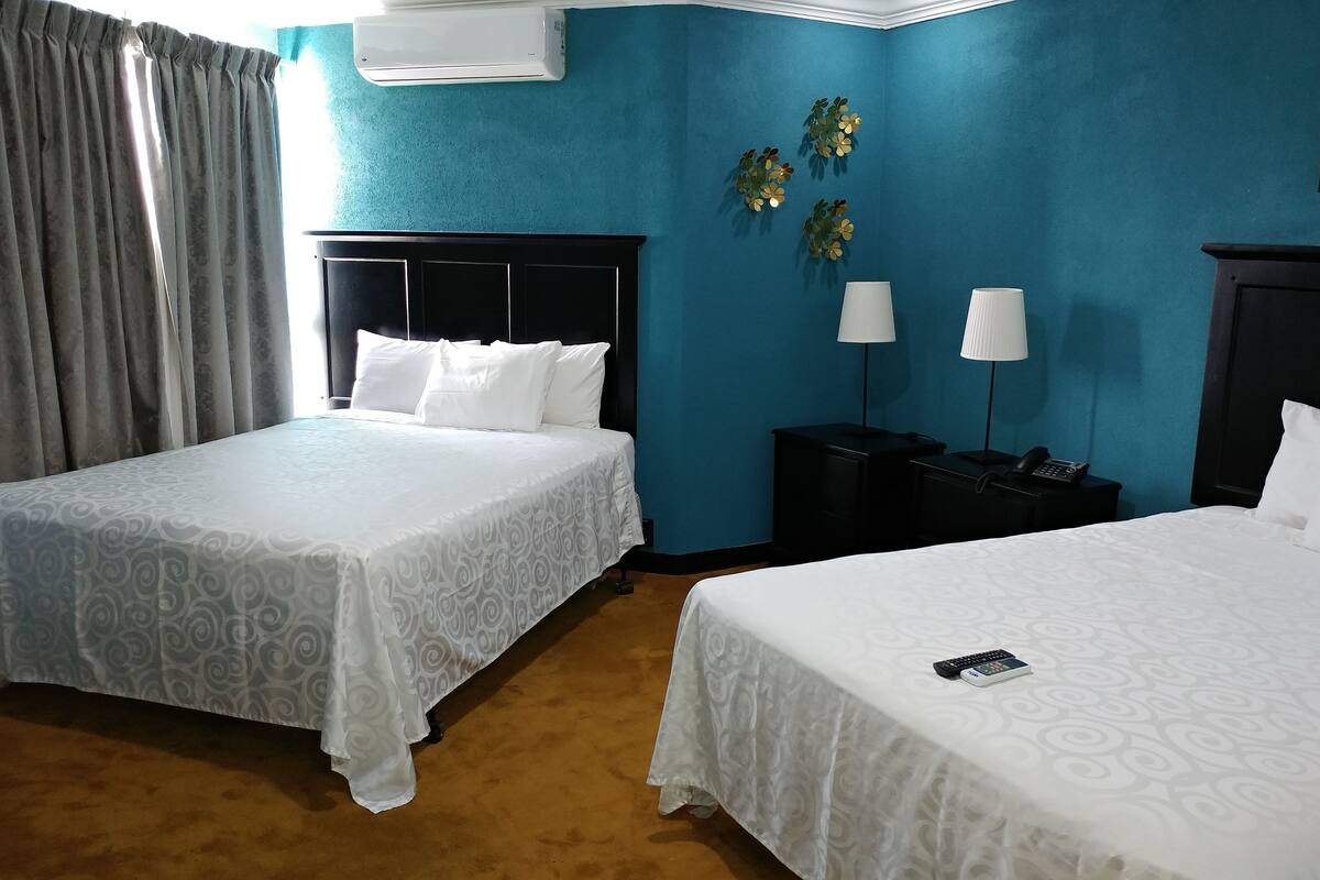 Een hotelkamer met twee bedden, een nachtkastje, een lamp en een wandairconditioner.