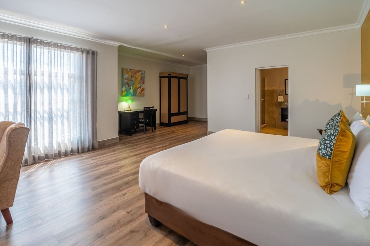 A hotel room with a large bed, a desk, a chair, and a painting on the wall.